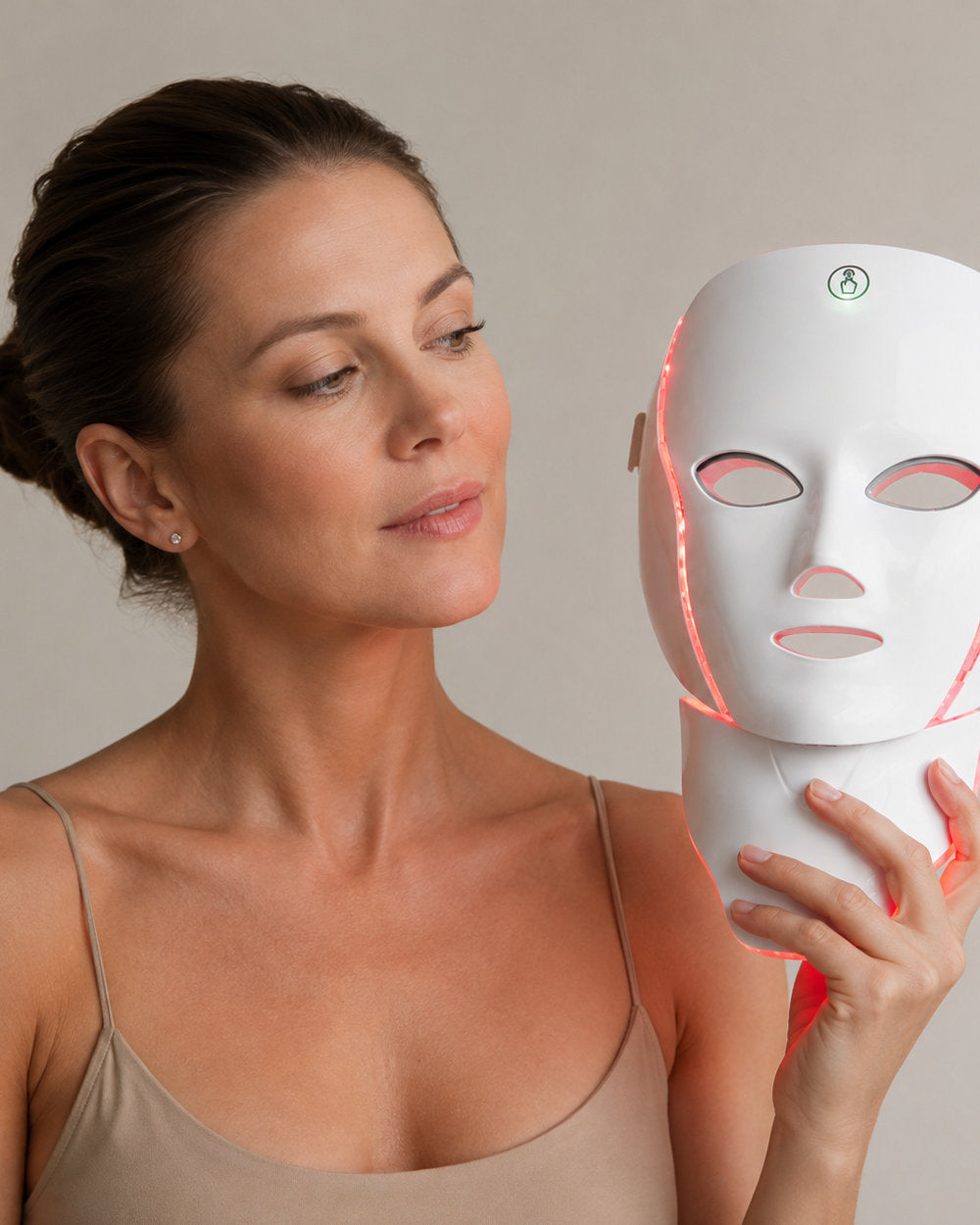 The LED Longevity Mask held in one hand, showing the face shell and the attached neck piece lit red